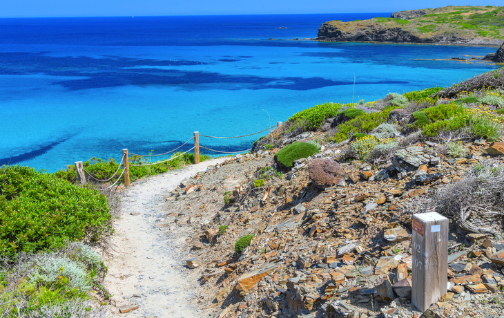 Wanderweg an felsiger Küste mit Blick auf klarblaues Meer.