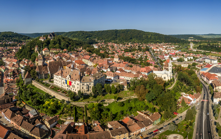 Panoramaansicht einer historischen Stadt mit Fluss und Hügellandschaft im Hintergrund.