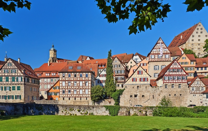 Fachwerkhäuser vor einer Stadtmauer unter blauem Himmel.