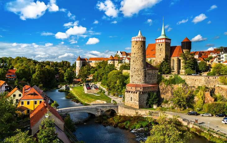 Mittelalterliche Stadt mit Fluss und Brücke unter blauem Himmel.