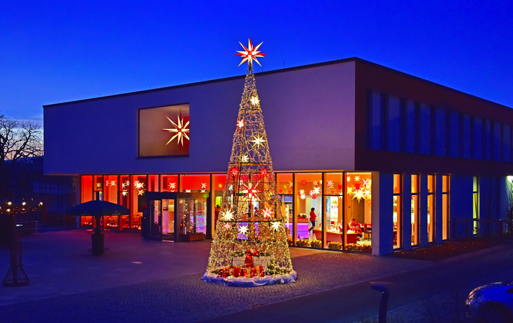 Gebäude der Herrnhuter Sterne Manufaktur mit beleuchtetem Weihnachtsbaum im Winter.