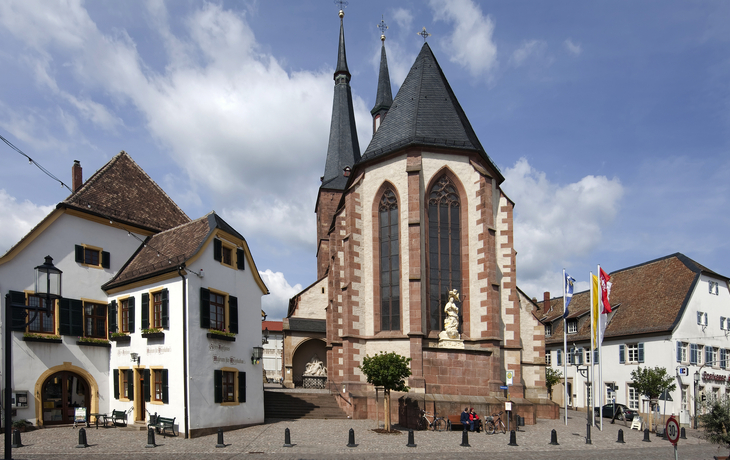 Stadtplatz mit Kirche und traditionellen Gebäuden bei blauem Himmel.