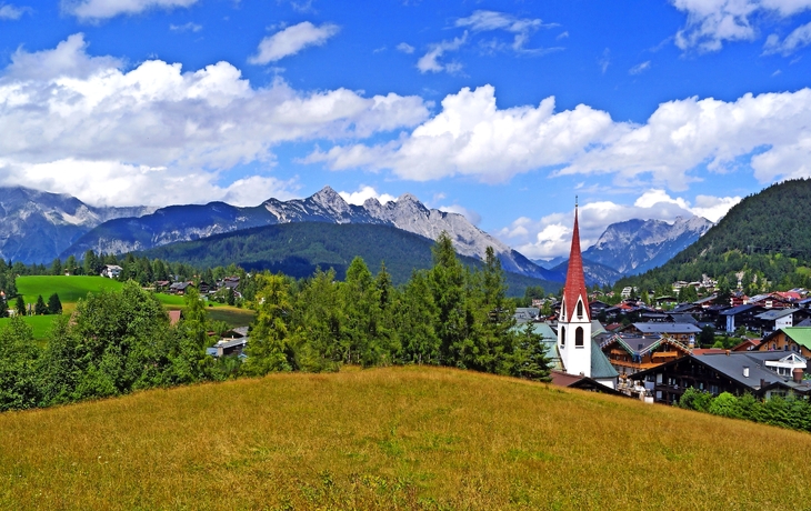 Berglandschaft mit Dorfkirche und Alpen im Hintergrund