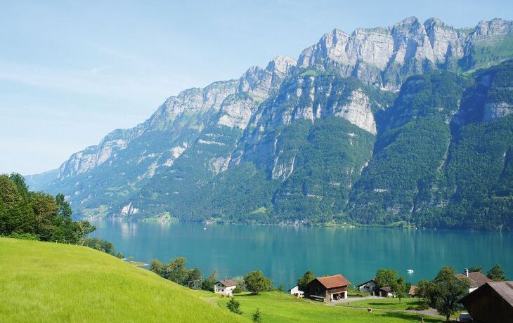 Berglandschaft mit See, grünen Wiesen und Häusern im Vordergrund.