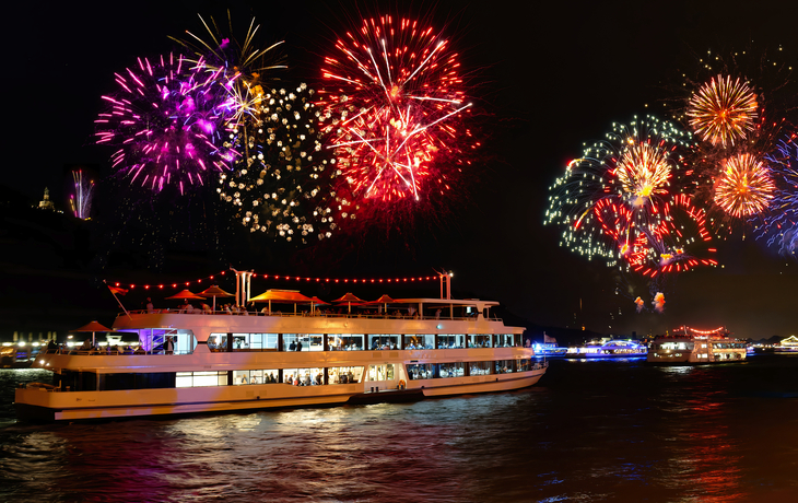 Schiff auf einem Fluss am Abend mit Feuerwerk am Himmel.