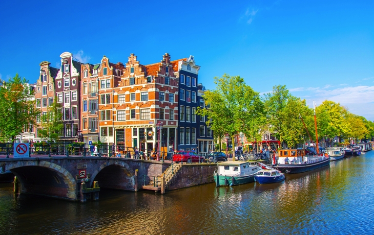 Kanal in Amsterdam mit Booten und alten Gebäuden bei sonnigem Wetter