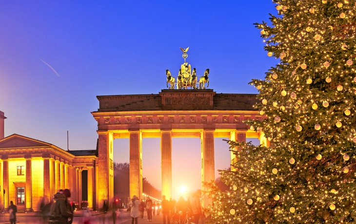 Brandenburger Tor bei Sonnenuntergang mit Weihnachtsbaum im Vordergrund.