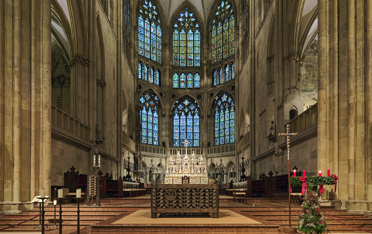 Innenraum einer gotischen Kathedrale mit bunten Glasfenstern und Altar.