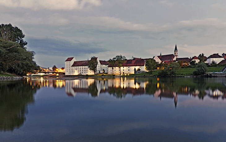 Abendlicher Blick auf historische Gebäude am Flussufer, im Wasser spiegelnd.