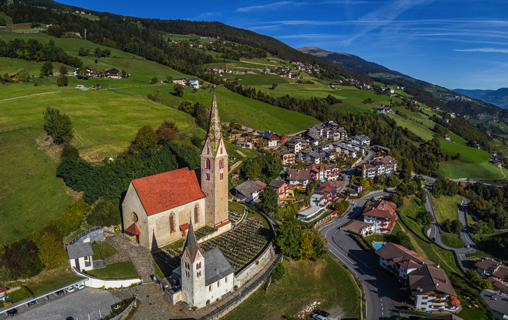 Luftaufnahme einer Kirche und Dorf in einer hügeligen Landschaft.