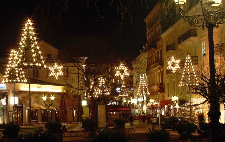 Straßenansicht mit weihnachtlicher Beleuchtung und geschmückten Bäumen bei Nacht.