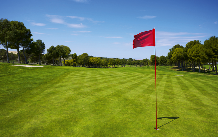 Roter Flaggenstock auf einem Golfplatz unter blauem Himmel