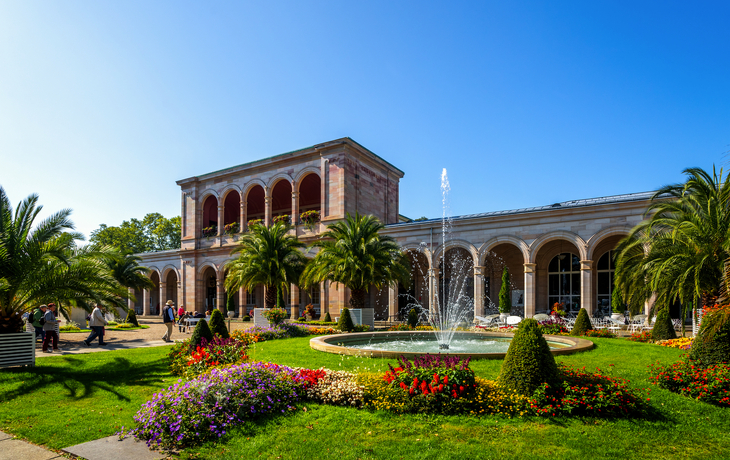Historisches Gebäude mit Arkaden, Brunnen und Garten.
