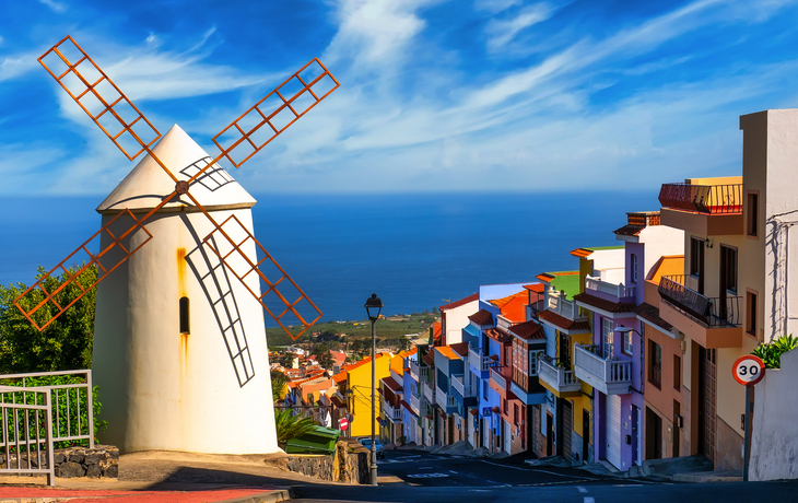 Windmühle auf Teneriffa mit bunten Häusern und Blick auf das Meer im Hintergrund.