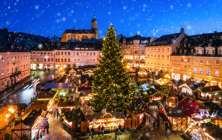 Festlich beleuchteter Weihnachtsmarkt bei Schneefall in historischem Stadtzentrum.