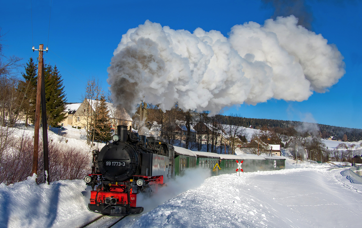 Dampflok der Fichtelbergbahn im winterlichen Schnee, blauer Himmel, rauchende Lokomotive.