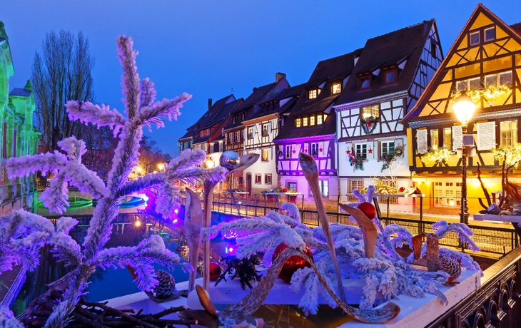 Verschneite Fachwerkhäuser und Dekorationen bei Nacht in Colmar, Frankreich.