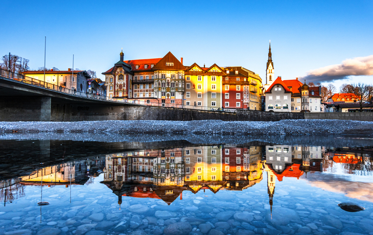 Stadtpanorama spiegelt sich in ruhigem Flusswasser bei klarem Himmel.