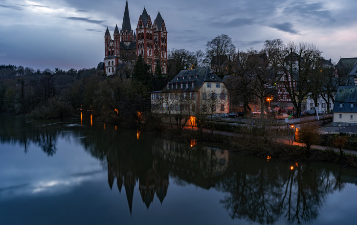 Blick auf eine beleuchtete Burg an einem See bei Abenddämmerung.