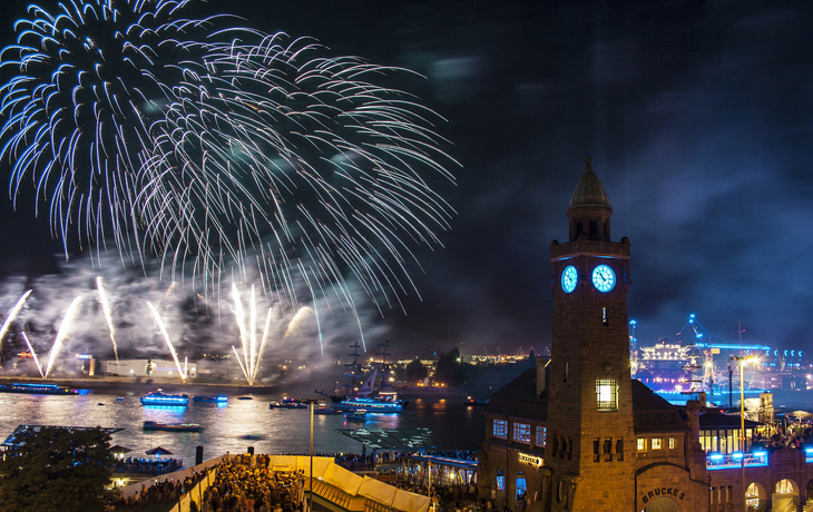 Feuerwerk über einem Fluss bei Nacht mit beleuchtetem Uhrturm im Vordergrund.