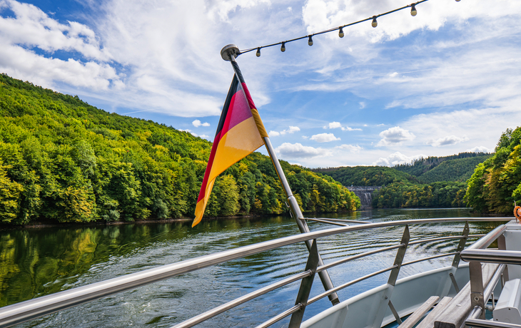 Bootsfahrt auf einem Fluss mit deutscher Flagge im Sommer.