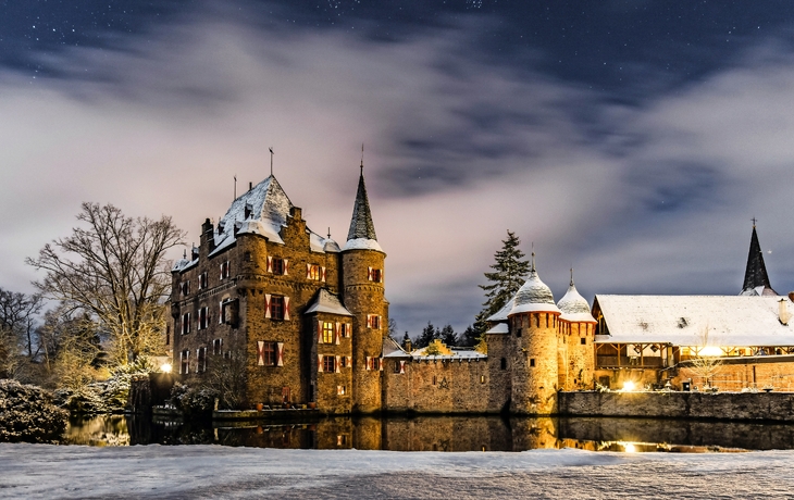 Schloss im Schnee bei Nacht mit beleuchtetem Innenhof