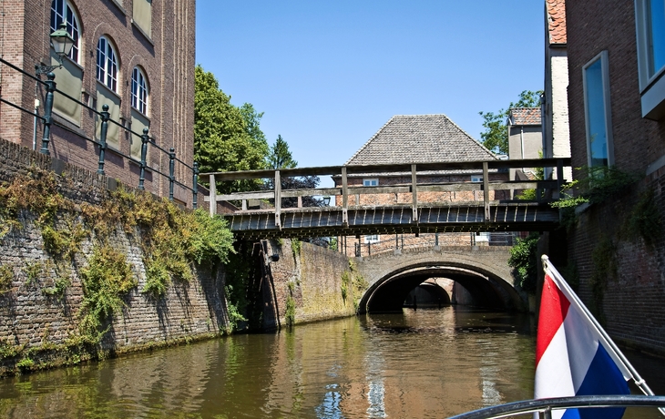 Kanal mit Backsteinhäusern und Brücke, niederländische Flagge im Vordergrund.