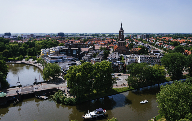 Stadtansicht mit Kirche, Fluss und Booten bei sonnigem Wetter.