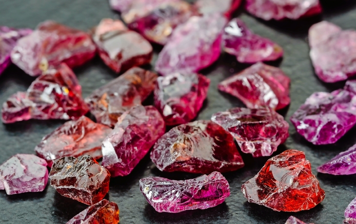 Rote und violette rohe Edelsteine, unpoliert und auf einer dunklen Oberfläche verstreut.