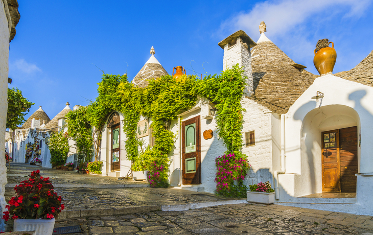 Traditionelle Trulli-Häuser mit bepflanzten Fassaden in sonnigem Dorf.