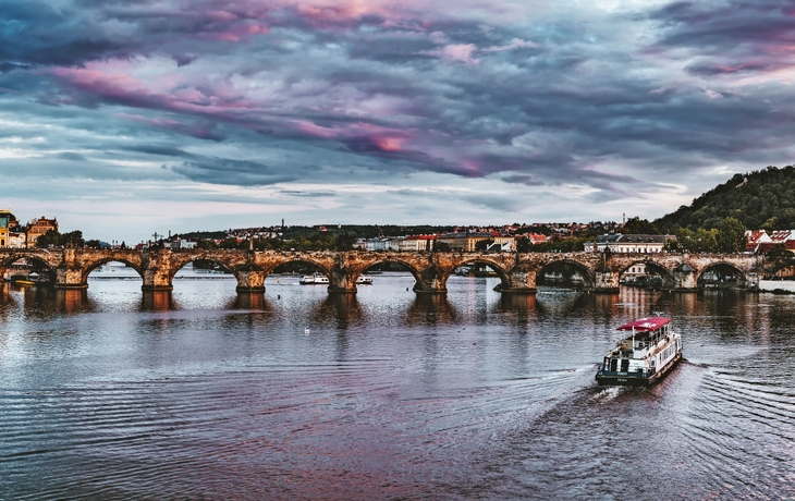 Stadtansicht mit historischer Brücke über Fluss, Boot auf dem Wasser, bewölkter Himmel.