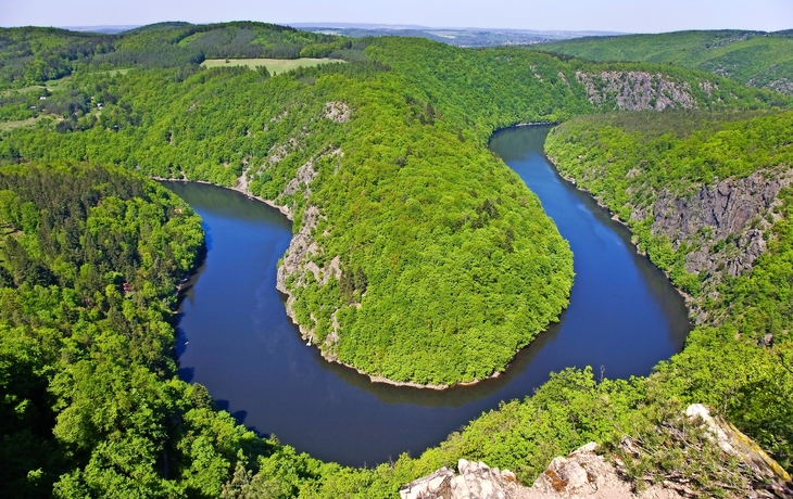 Fluss, der sich durch eine bewaldete Landschaft windet, umgeben von grünen Hügeln.