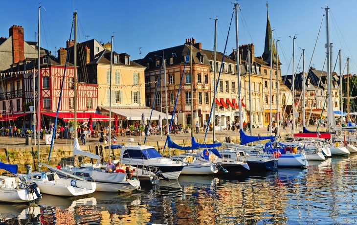 Hafen mit Segelbooten und historischen Gebäuden im Hintergrund bei Sonnenuntergang.