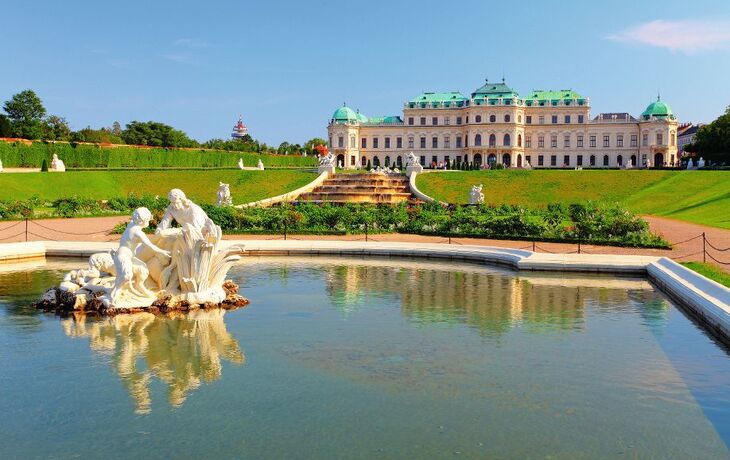 Barockes Schloss mit Gartenanlage und Teich im Vordergrund.