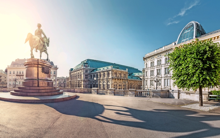 Reiterstatue auf großem Platz vor historischen Gebäuden bei Sonnenschein.