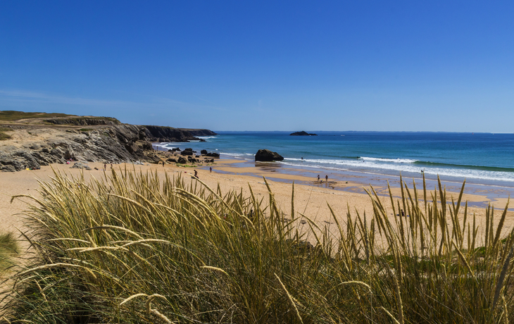 Sandstrand mit Felsen und klarem blauen Himmel im Hintergrund.