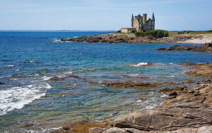 Küste mit Felsen und einem Schloss im Hintergrund am Meer.