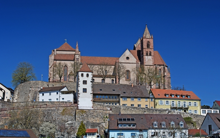 Kirche auf einem Hügel mit Wohnhäusern im Vordergrund unter klarem blauem Himmel.