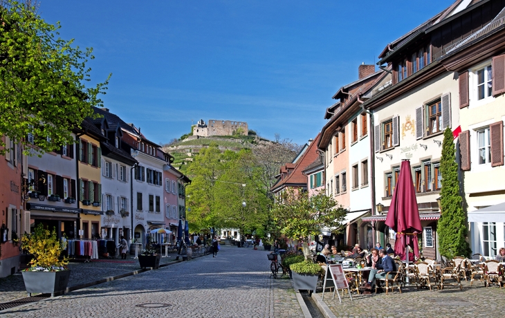 Eine Kopfsteinpflasterstraße mit Cafés, umgeben von historischen Gebäuden.
