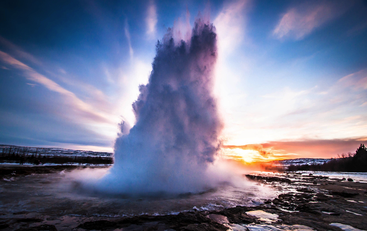 Geysir-Ausbruch bei Sonnenuntergang mit dramatischem Himmel.