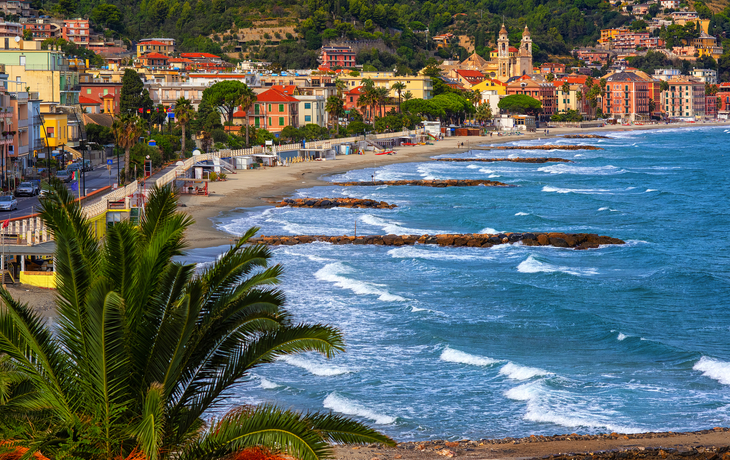 Küstenansicht einer italienischen Stadt mit Strand und Wellen im Vordergrund.