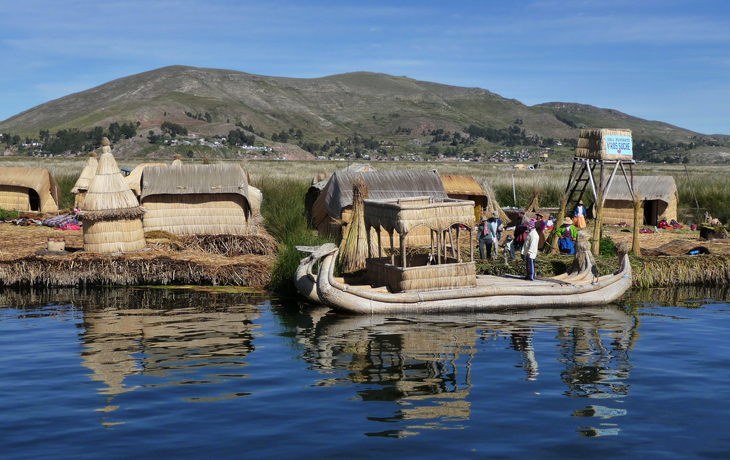 Menschen auf schwimmenden Schilfinseln mit Boot auf einem See vor Berglandschaft.