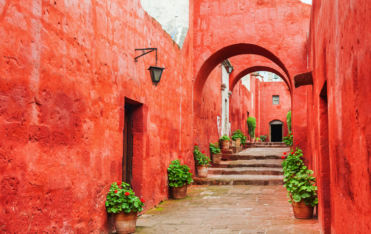 Rote Gasse mit Bögen und Pflanzen in Töpfen, sonniger Tag