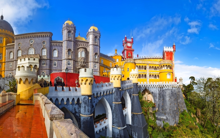 Buntes Schloss auf Hügel mit blauen Himmel und grüner Landschaft.