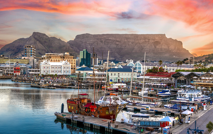 V&A Waterfront in Kapstadt, Südafrika, mit Hafen und Tafelberg im Hintergrund bei Sonnenuntergang.