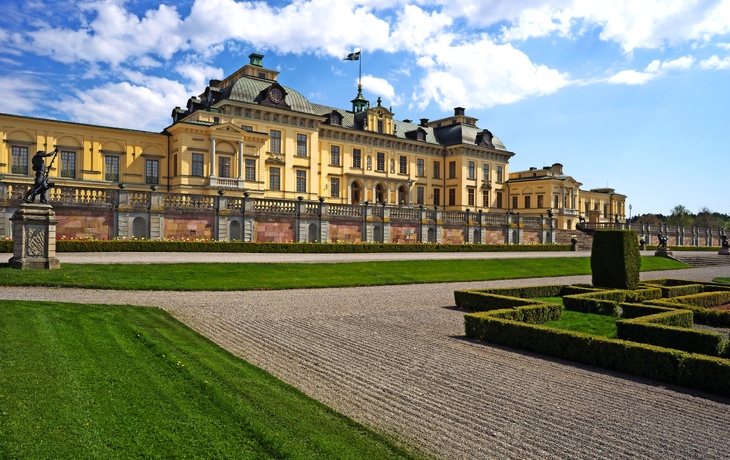 Gelbes Schloss mit formellen Gärten im Vordergrund bei blauem Himmel.