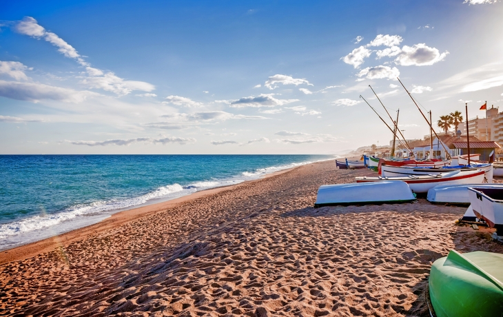 Strand mit mehreren Fischerbooten auf dem Sand mit blauem Meer und Himmel im Hintergrund.