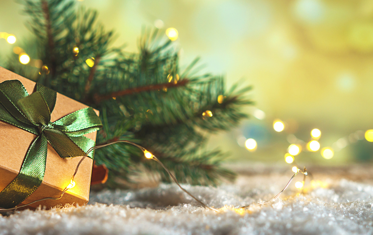 Weihnachtliches Geschenk mit grünem Band vor Tannenzweigen und Lichtern