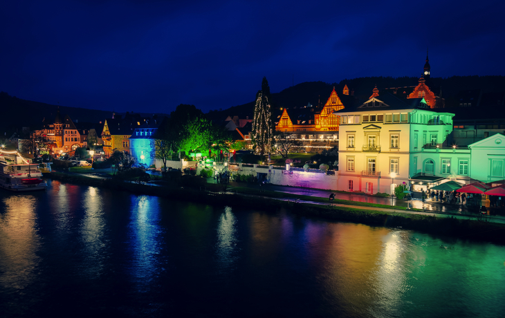 Abendliche Stadtansicht mit bunten Lichtern am Flussufer.