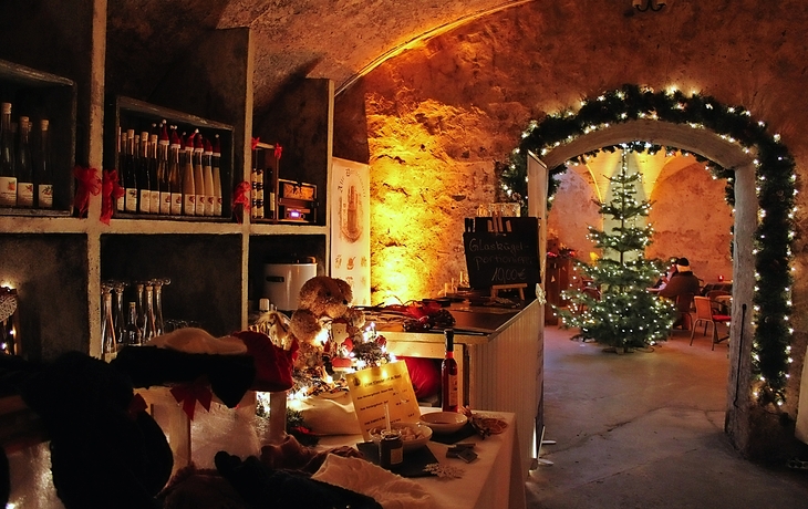 Weihnachtsdeko in einem Weinkeller mit erleuchtetem Weihnachtsbaum im Hintergrund.